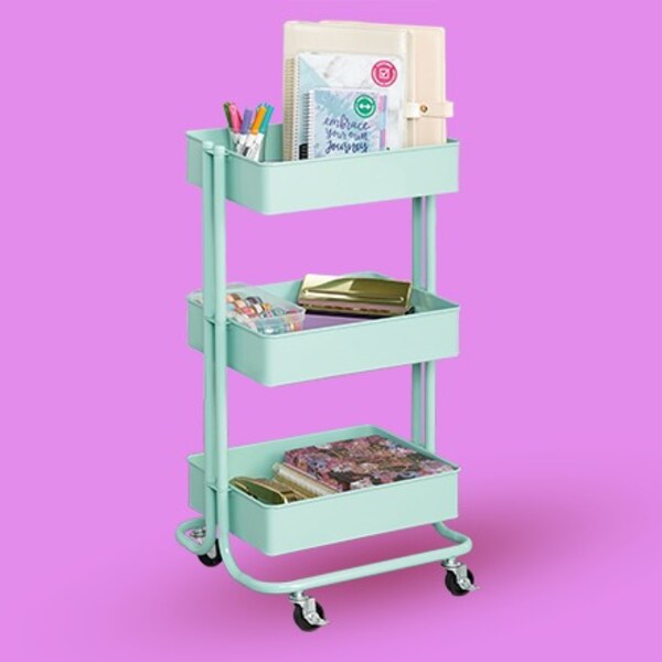 tiered rolling cart with office accessories on purple background